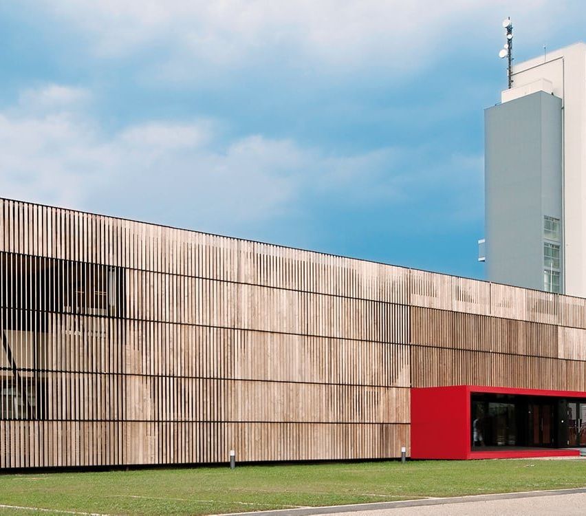 Ein modernes Gebäude mit einer Holzfassade und einem roten Eingangskasten an einem sonnigen Tag.