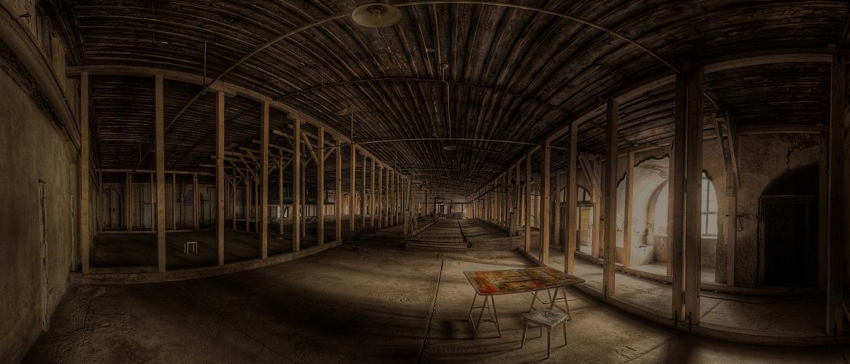 Ein leeres, altes Industrielagerhaus mit Holzbalken und Säulen, mit einem einzelnen Tisch und Hocker im Vordergrund.