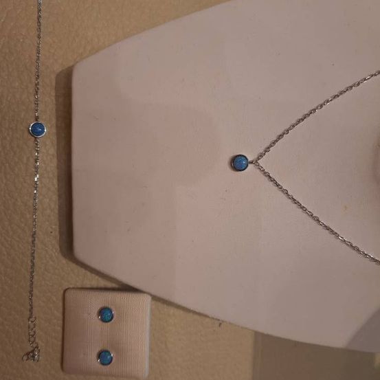 Eine Silberkette mit blauen Edelsteinen wird auf einer weißen Oberfläche präsentiert. Es gibt auch eine Silberarmband und eine kleine Box mit blauen Edelsteinen.