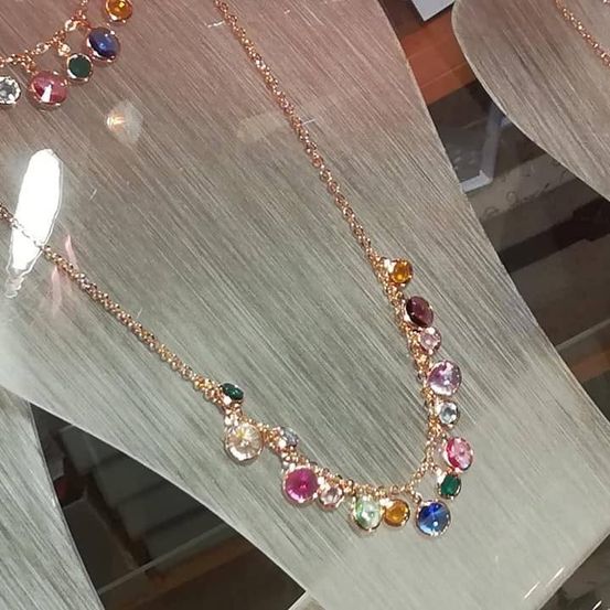 Eine Halskette mit bunten Edelsteinen wird ausgestellt. Die Halskette ist gold mit einer Mischung aus rosa, grünen, blauen und gelben Steinen.