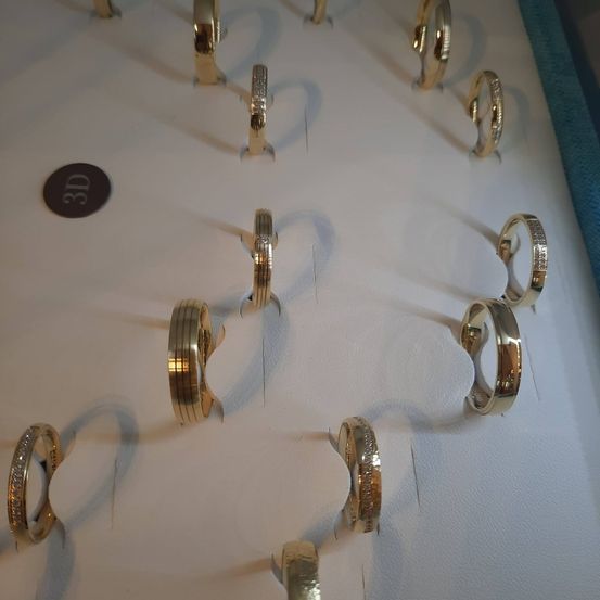 Eine Sammlung von Goldringen, einschließlich Ehe- und Ewigkeitsringe, ist auf einer weißen Oberfläche ausgestellt. Jeder Ring ist sorgfältig gefertigt und weist eine polierte Oberfläche auf. Einige Ringe haben Diamantakzente.
