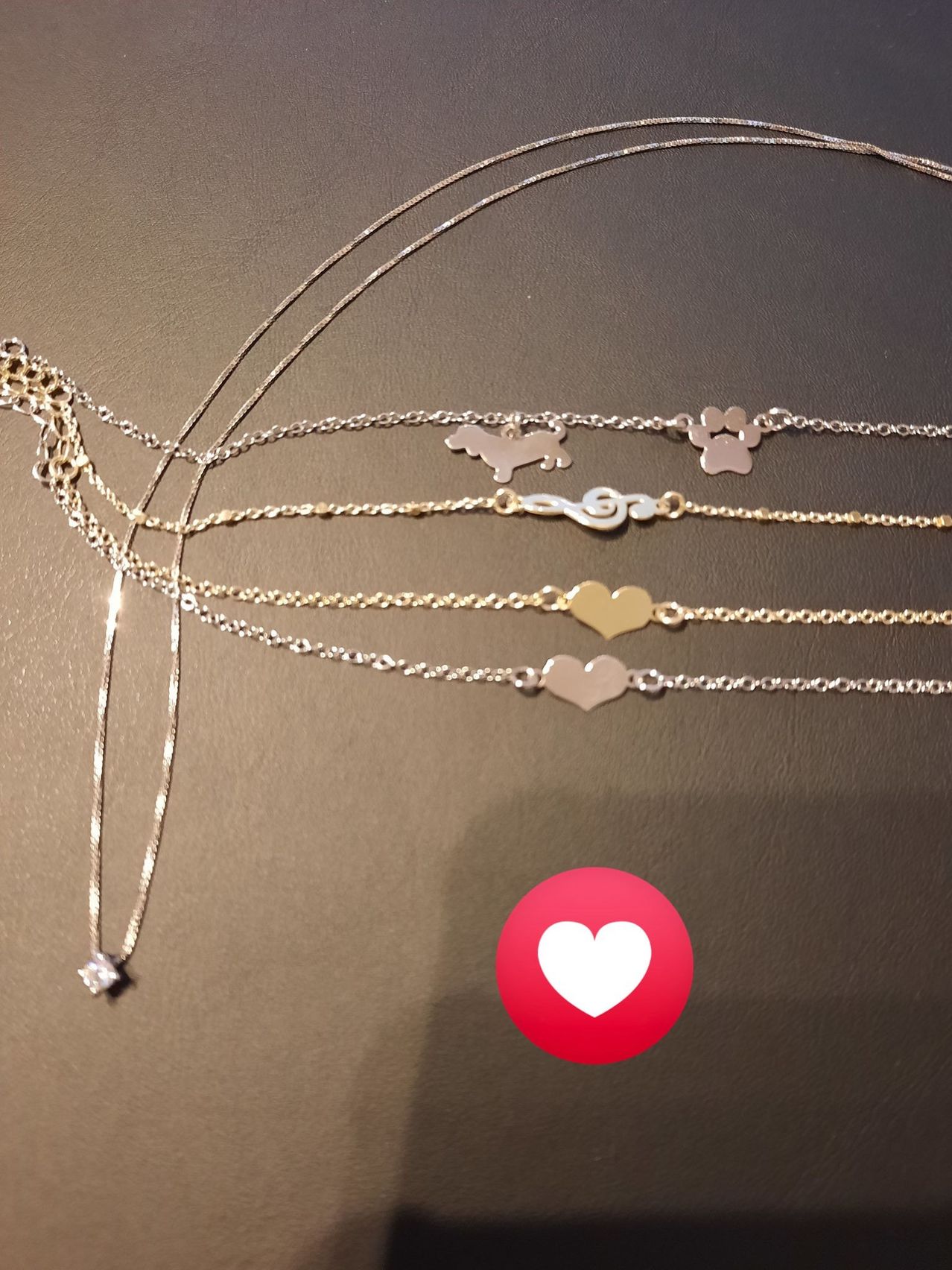 Fünf Halsketten mit verschiedenen Designs sind auf einem braunen Hintergrund zu sehen. Die Designs umfassen einen Pfotenabdruck, einen Hund, eine musikalische Note und zwei Herzanhänger.