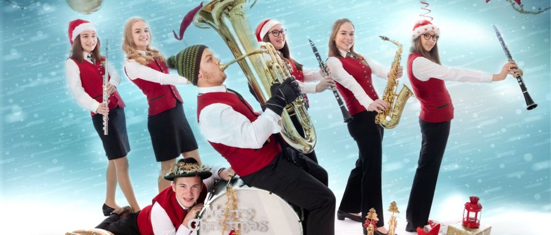 Eine fröhliche Musikgruppe in roten und weißen Uniformen und Weihnachtsmützen posiert mit Instrumenten vor einem verschneiten Hintergrund. Die zentrale Figur spielt Tuba, während andere Saxophone, Flöten und Trommeln spielen.