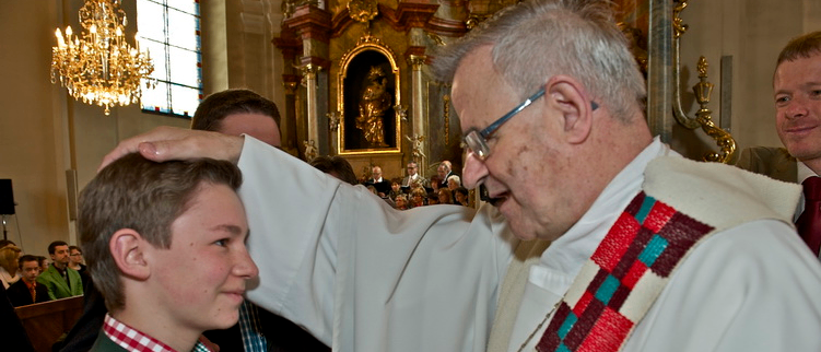 Ein Priester in einer Kirche legt seine Hand auf den Kopf eines lächelnden Jungen.