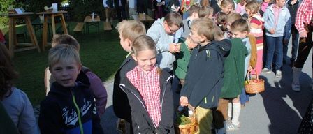 Eine Gruppe von Kindern und Erwachsenen versammelt sich vor einem Gebäude. Einige Kinder halten Körbe mit Erdbeeren. Die Erwachsenen stehen im Hintergrund.