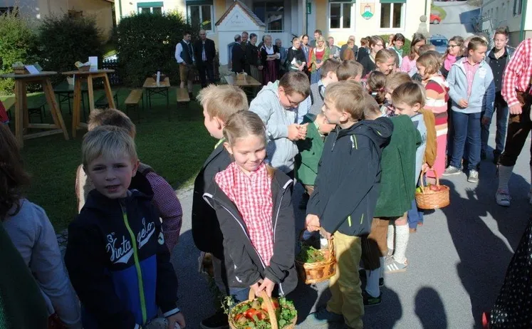 Eine Gruppe von Kindern und Erwachsenen versammelt sich vor einem Gebäude. Einige Kinder halten Körbe mit Erdbeeren. Die Erwachsenen stehen im Hintergrund.