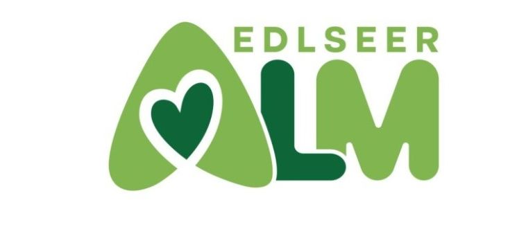 Das Logo der Edlseeer Alm zeigt ein grünes Herz in einem Dreieck mit 'EDLSEER' darüber und 'LM' darunter, alles in Grün auf weißem Hintergrund.