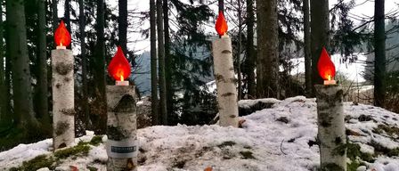 Zwei rote Kerzen auf Birkenstämmen stehen in einem verschneiten Wald. Der Boden ist schneebedeckt.
