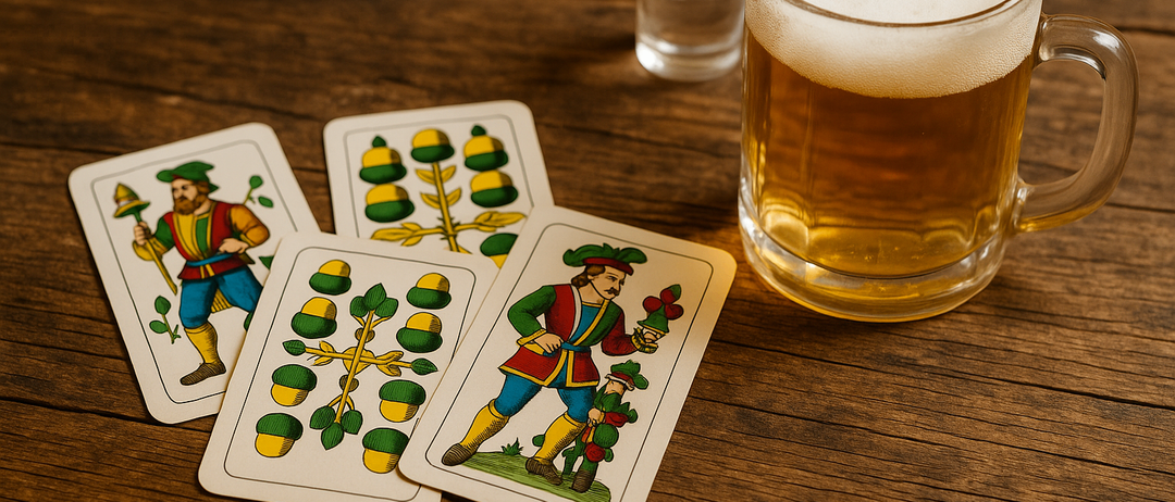 Vier Spielkarten liegen auf einem Holztisch neben einem Glas Bier und einem Schnapsglas. Die Karten haben verschiedene Designs, eine hat einen Mann in Hut und Blume.