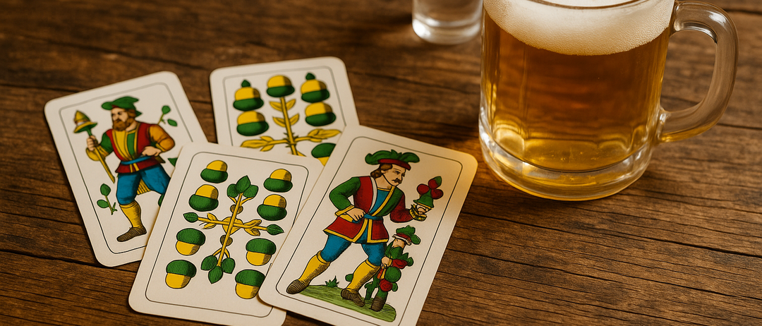 Auf einem Holztisch stehen ein Glas Bier, ein kleines Schnapsglas und vier Karten mit grünen und gelben Designs. Die Karten haben verschiedene Illustrationen, darunter einen Mann und einen Baum.