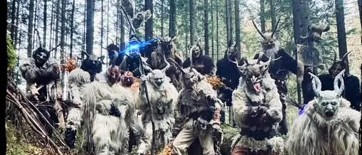 Eine Gruppe von Menschen in Kostümen mit Hörnern und Masken posiert in einem Wald mit einem Feuer im Vordergrund. Der Text 'Joglllandteif' und 'Seit 2007' ist sichtbar.
