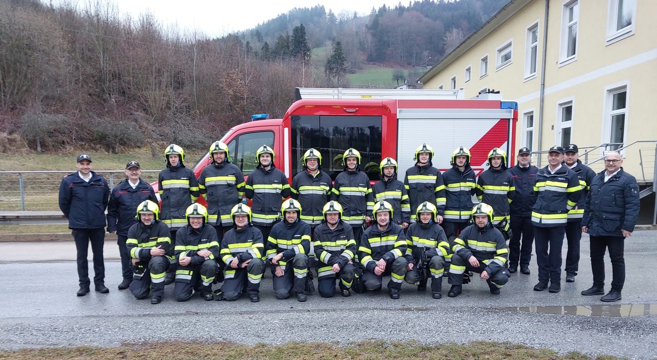 Eine Gruppe Feuerwehrleute in Uniformen posiert für ein Foto vor einem Feuerwehrauto mit einem Berg im Hintergrund.