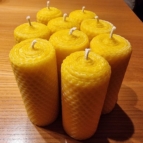 Acht gelbe Bienenwachskerzen sind auf einem Holztisch angeordnet. Die Kerzen haben ein Wabenmuster und weiße Dochte.