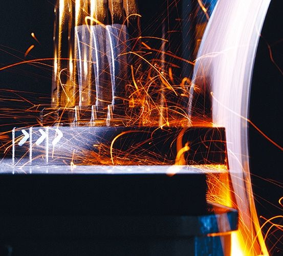 Eine Nahaufnahme einer Metallbearbeitungsmaschine mit Funkenflug aus dem Schneidprozess. Die Maschine ist von einem hellen Licht beleuchtet, das Schatten auf die Metallteile wirft.