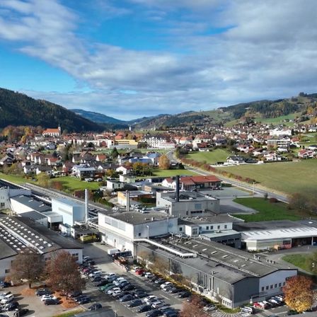 Eine Luftaufnahme einer Stadt mit vielen Gebäuden, einer großen Fabrik und einem Parkplatz mit vielen geparkten Autos.