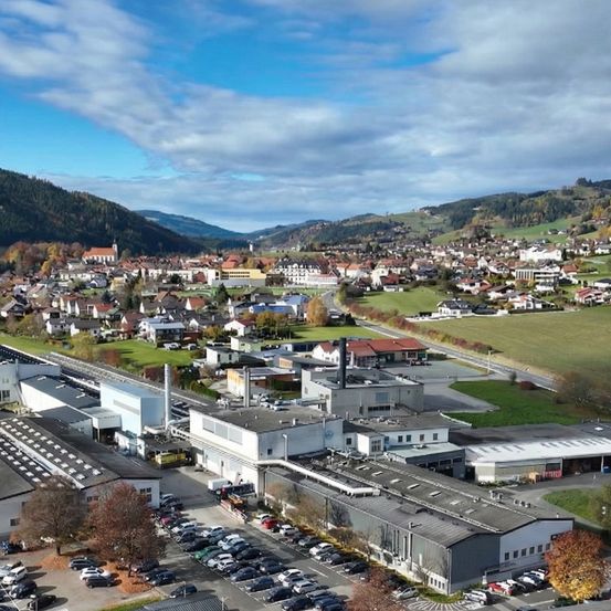 Eine Luftaufnahme einer Stadt mit vielen Gebäuden, einer großen Fabrik und einem Parkplatz mit vielen geparkten Autos.