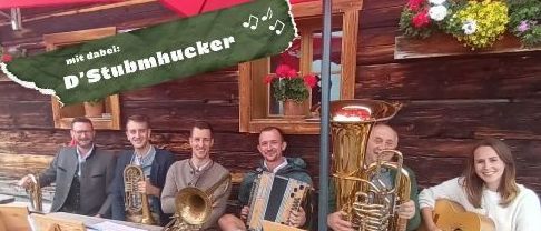 Eine Band mit Blechblasinstrumenten und einem Gitarristen posiert vor einem Holzgebäude. Das Bild hat eine festliche Überlagerung mit Noten.