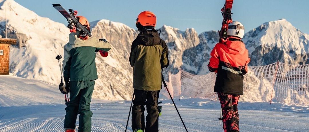 Drei Kinder in Skiausrüstung gehen auf einem verschneiten Hang, mit Bergen im Hintergrund. Das Poster bewirbt ein Familienfest mit Erlebnisstationen. Datum: 8. März 2026, Beginn um 10:00 Uhr.