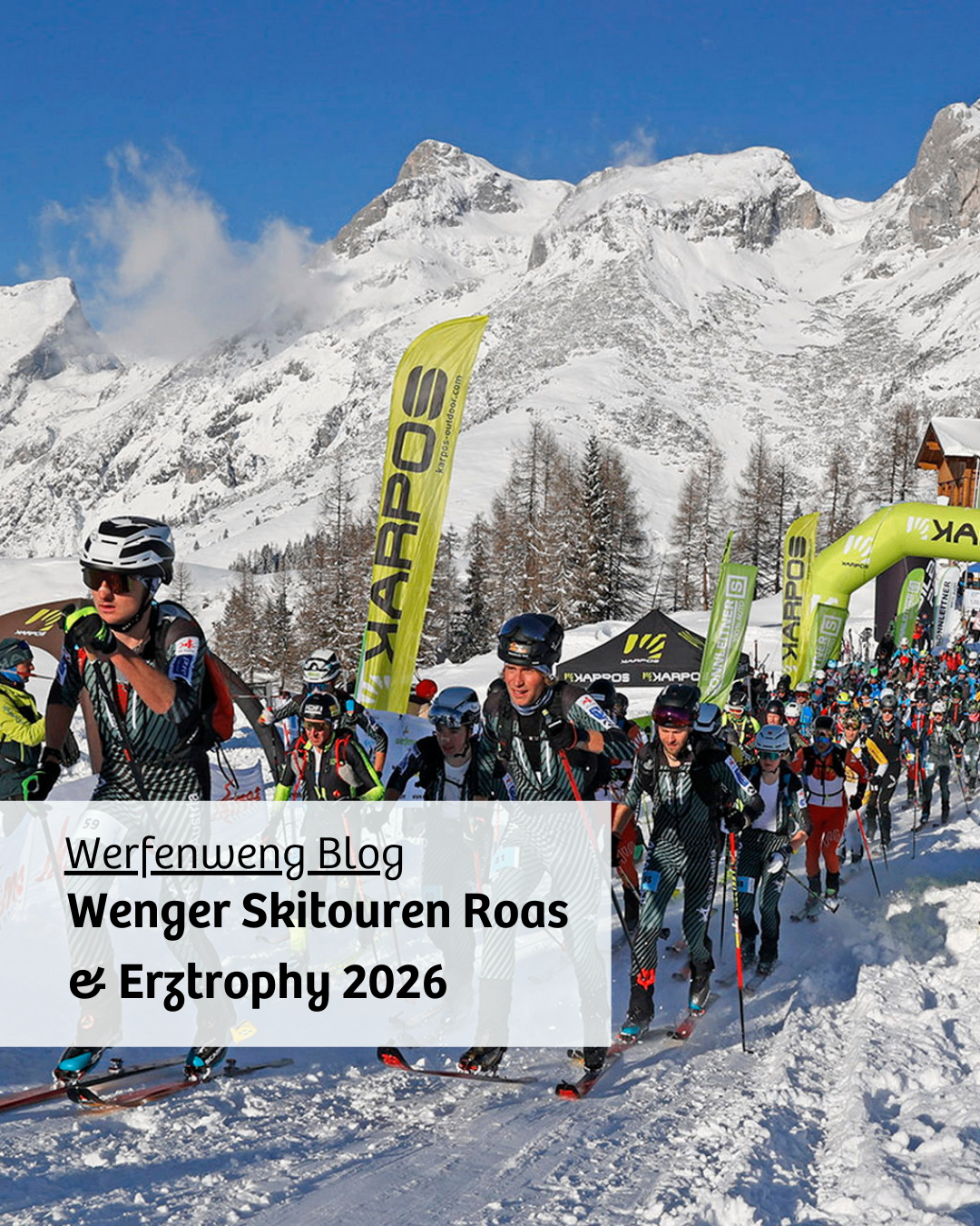 Skiers in helmets and ski suits are participating in a ski tour event, with mountains in the background and flags along the side.