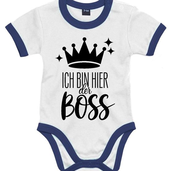 Weißes Baby-Bodysuit mit blauer Einfassung. Über dem Text 'ICH BIN HIER DER BOSS' befinden sich eine schwarze Krone und Sterne.