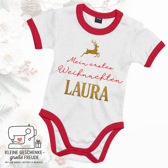 Ein weißes und rotes Babybodysuit mit 'Mein erstes Weihnachten LAURA' und einer goldenen Rehen-Illustration.