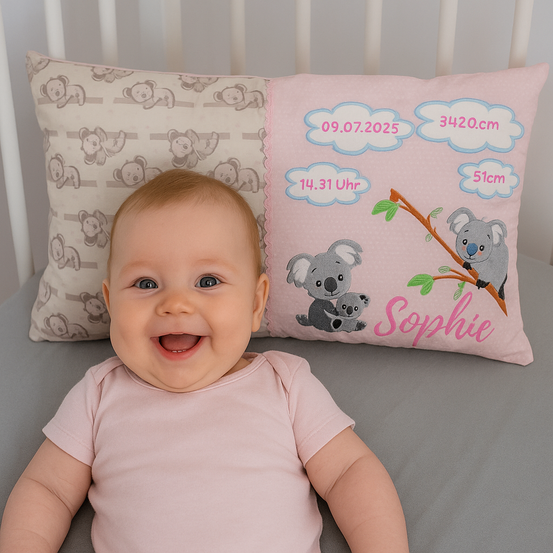 Ein Babymädchen namens Sophie liegt auf einem Bett mit zwei Kissen. Ein Kissen hat eine Koala-Familie darauf und das andere hat Bärenbilder.