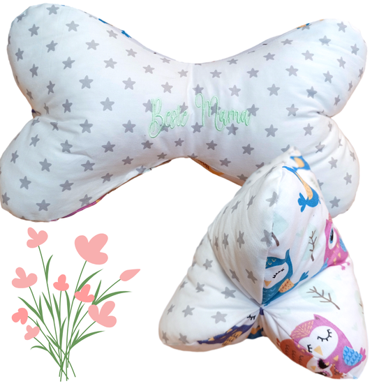 Zwei Kissen mit Sternenmustern, eines sagt 'Beste Mama'. Ein Kissen zeigt Eulen und ein anderes bunte Vögel. Ein Strauß rosa Blumen ist ebenfalls vorhanden.