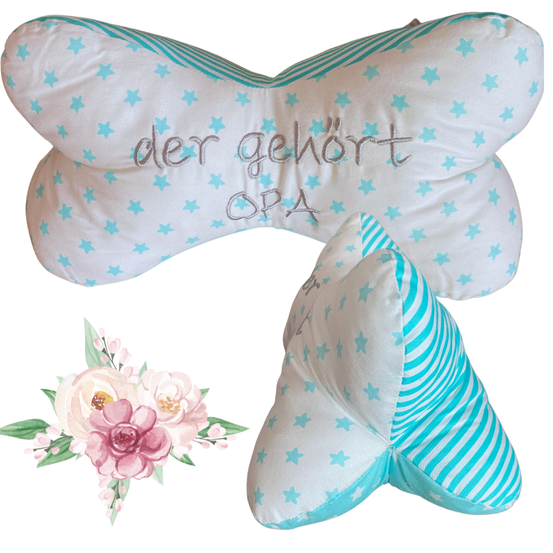 Zwei kissenförmige Plüschtiere mit blauen Sternen und Streifen. Eines hat den Text 'der gehort OPA' und das andere hat ein blaues Sternmuster. Im Hintergrund befindet sich auch eine Blumenarrangement.