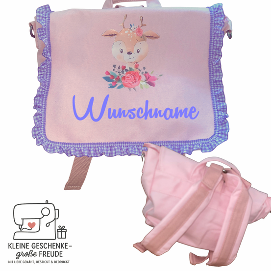 Ein rosa Rucksack mit einer Hirschillustration und Blumen, personalisiert mit dem Namen 'Wunschname'. Der Rucksack liegt auf einem weißen Hintergrund. Unter dem Rucksack befindet sich ein Logo mit einer Nähmaschine und einem Geschenk.