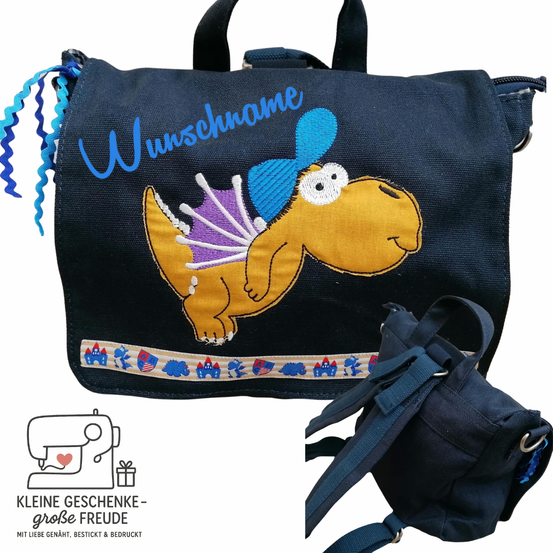 Ein blauer Rucksack mit einem Dinosaurier-Design und dem Wort 'Wunschname' darauf. Unten ist ein kleinerer blauer Rucksack zu sehen. Ein Logo mit einer Nähmaschine und einem Herz befindet sich unten links.