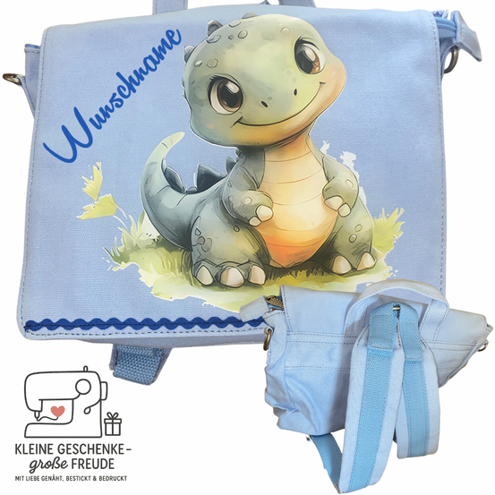 Ein blauer Rucksack mit einem Cartoon-Dinosaurier, der auf Gras sitzt. Der Rucksack hat einen Namen 'Unsname' und eine kleine Tasche. Der Dinosaurier lächelt und hat ein gelbes Blatt neben sich.