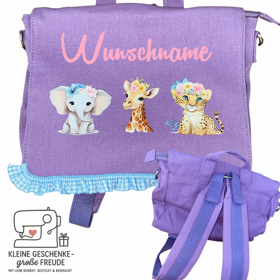 Ein lila Rucksack mit einem weißen Elefanten, einer Giraffe und einem Leoparden mit Blumen im Haar. Das Wort 'Wunschname' ist in Pink geschrieben. Es gibt auch eine kleinere lila Tasche.