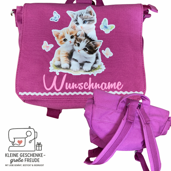 Ein rosa Rucksack mit drei Kätzchen und Schmetterlingen darauf. Unter den Kätzchen steht der Text 'Wunschname'. Daneben liegt eine kleinere rosa Tasche.