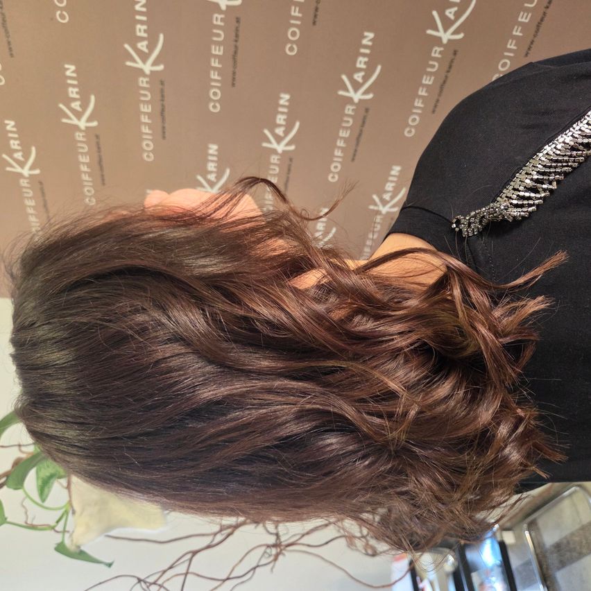 Ein Nahaufnahme einer Frau mit braunen, gewellten Haaren, die in einem Salon nach unten schaut.