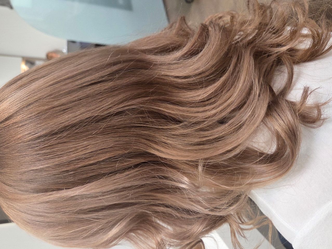 Eine Nahaufnahme von langen, welligen, hellbraunen Haaren mit einem weichen, natürlichen Look. Das Haar ist voluminös und erscheint glänzend.