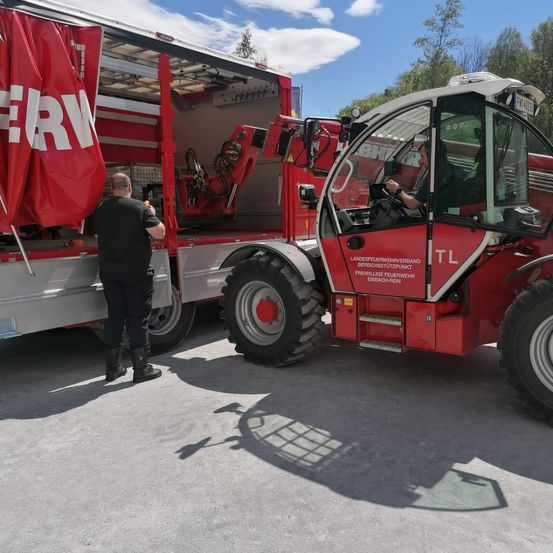 Ein Feuerwehrfahrzeug steht auf der Straße. Ein Mann steht neben dem Fahrzeug. Eine rote Fahne hängt an der Seite des Fahrzeugs.