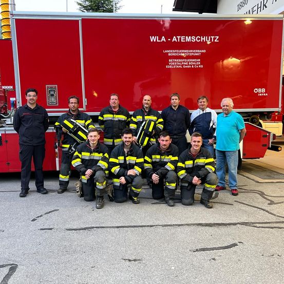 Eine Gruppe von Feuerwehrleuten posiert vor einem roten Feuerwehrauto mit Text darauf.