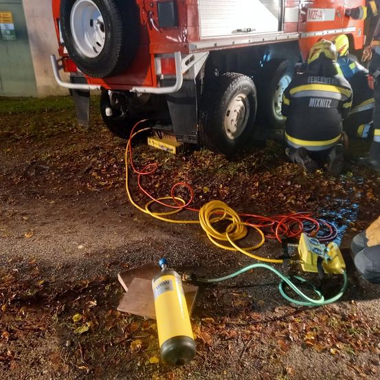 Feuerwehrleute arbeiten bei Nacht an einem Fahrzeug mit Kabeln und Ausrüstung auf dem Boden.