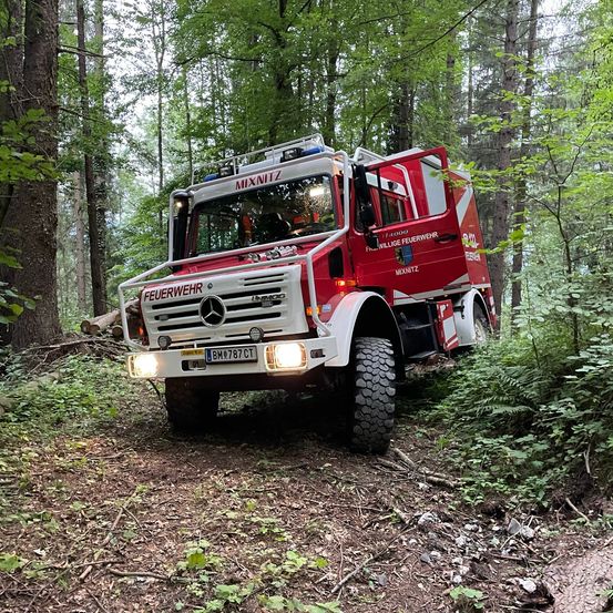 Ein roter Mercedes-Benz Feuerwehrwagen mit dem Kennzeichen BM 787 CT steht auf einem Waldweg.