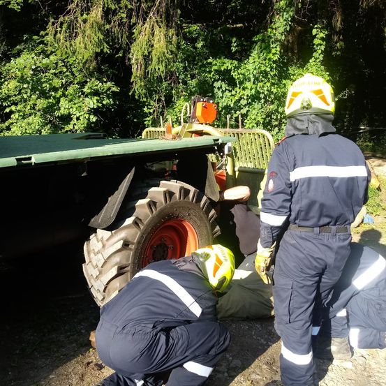 Ein Rettungsteam hilft einer Person, die unter einem großen Traktor eingeklemmt ist, wobei eine Person den Reifen untersucht.