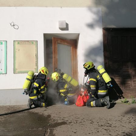 Drei Feuerwehrleute in gelben Helmen und gelben Uniformen knien auf dem Bürgersteig. Sie scheinen sich auf einen Notfalleinsatz vorzubereiten.