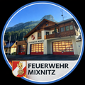 Das Bild zeigt die Feuerwehr Mixnitz mit einem Berg im Hintergrund, mit dem Logo und Wappen des Gebäudes, roten Türen und Fenstern, die den Himmel widerspiegeln.