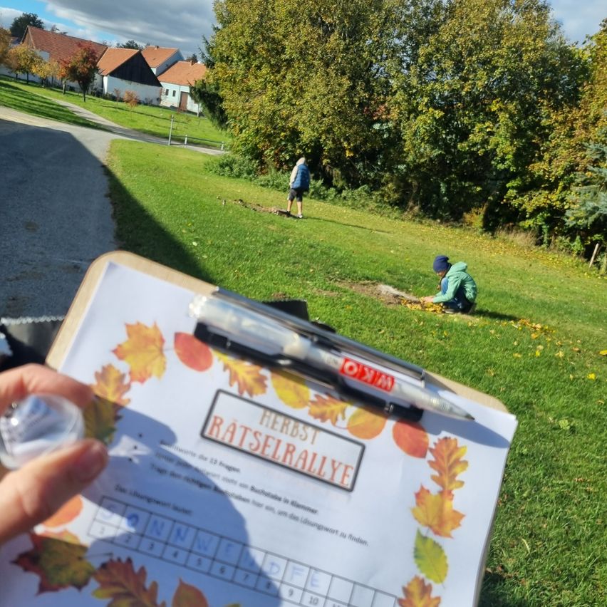 Eine Person hält einen Klemmbrett mit einem Raster und einem Stift. Zwei Kinder sind draußen auf einem Grasfeld. Eines kauert sich, während das andere steht.