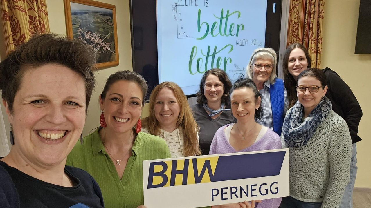 Eine Gruppe von Frauen lächelt und posiert für ein Foto mit einem Schild, auf dem BHW Pernegg steht, vor einer Beamerleinwand mit inspirierendem Text.