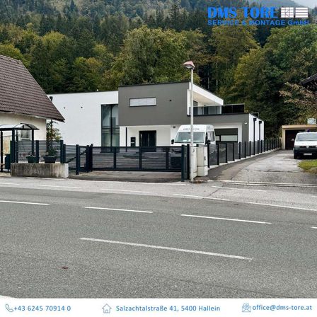 Ein Bild eines modernen Hauses mit einem schwarzen Zaun und einem weißen Van, der davor geparkt ist. Hinter dem Haus befinden sich Bäume und Berge. Unten sind Kontaktdaten und eine E-Mail-Adresse angegeben.