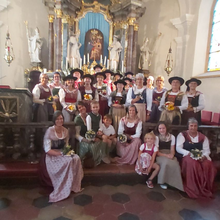 Eine Gruppe von Menschen in traditioneller Kleidung posiert für ein Foto in einer Kirche, mit einem geschmückten Altar und Statuen im Hintergrund.