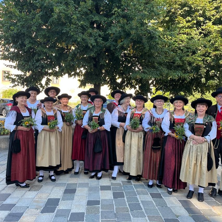 Eine Gruppe älterer Frauen in traditioneller Kleidung, die Blumen halten, posiert für ein Foto vor einem Baum.