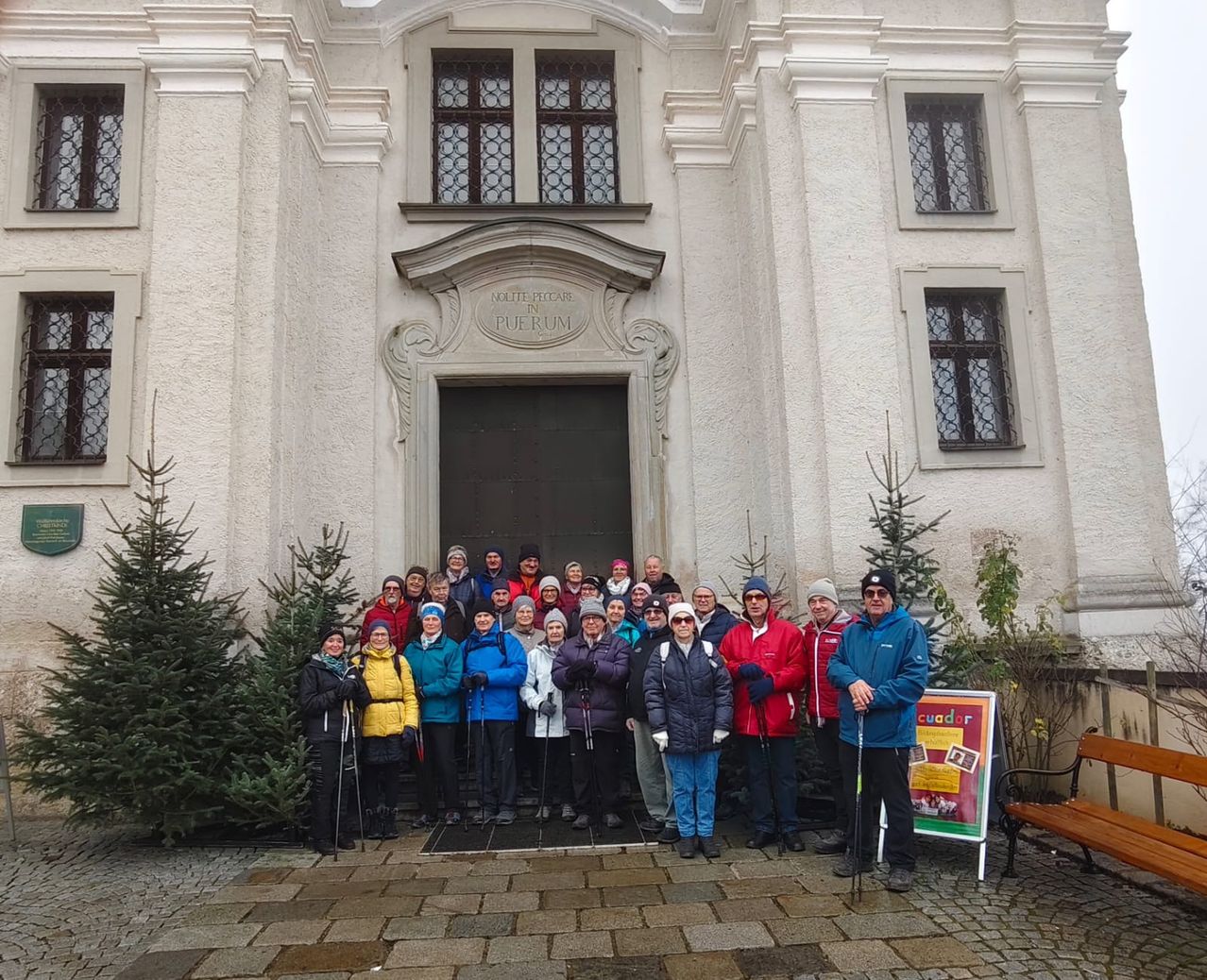 Eine Gruppe von Menschen in Winterkleidung steht vor einem Gebäude mit einer großen Holztür, geschmückt mit Weihnachtsbäumen.