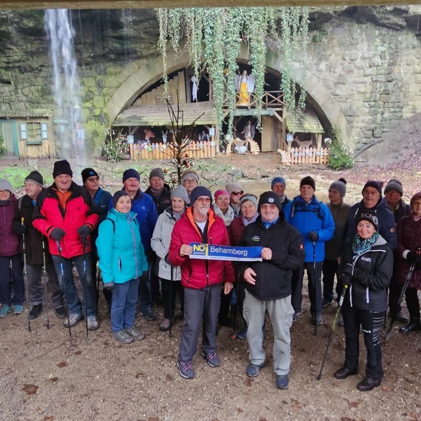 Eine Gruppe von Menschen in Winterkleidung posiert für ein Foto vor einem Wasserfall mit einem Höhleneingang.