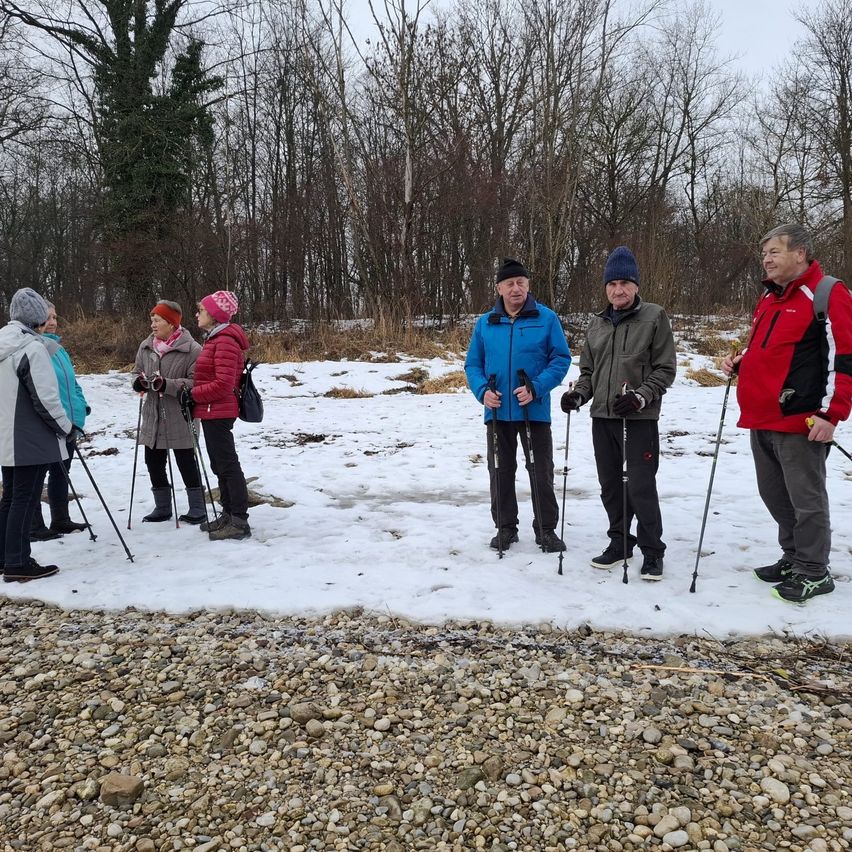 Eine Gruppe von Menschen steht auf einem verschneiten Pfad und hält Skistöcke. Sie sind in Winterkleidung gekleidet und scheinen eine Wanderung zu unternehmen. Bäume umgeben das Gebiet.